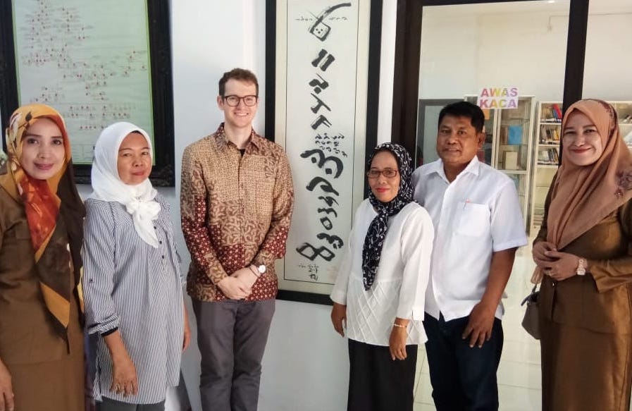 Six people standing in front of calligraphy. Michael Miller with archivists and friends at the regional archives office in Makassar, Indonesia