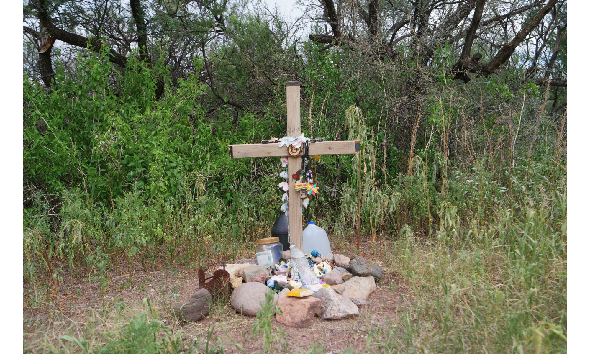 A makeshift memorial cross surrounded by rocks, trinkets, gifts, and water jugs.