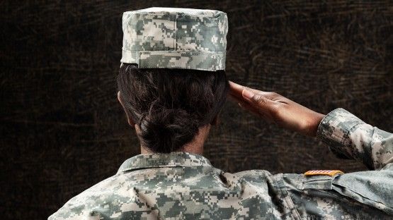 Woman soldier in military uniform stands at salute (seen from back of head)