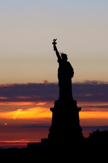 silhouette of Lady Liberty in New York City harbor at sunset
