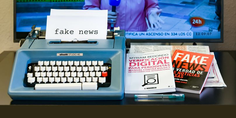 type writer with paper loaded that reads "fake news" and books about disinformation in the media 