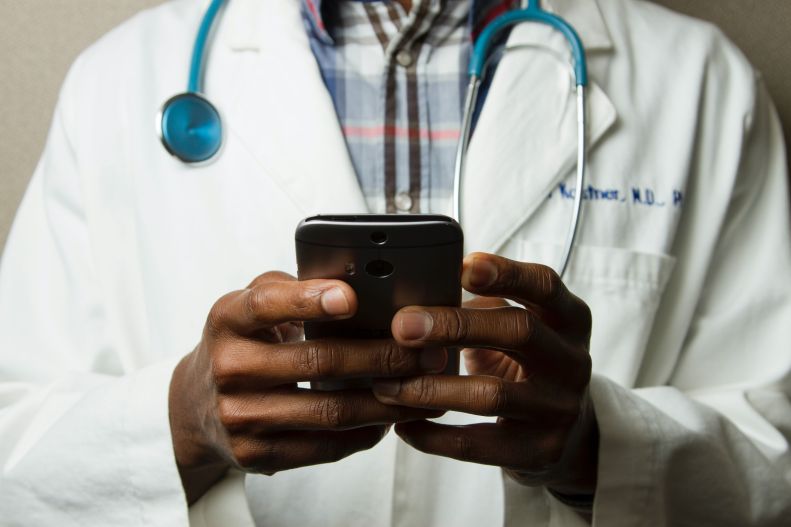 Doctor in lab coat wears stethoscope and holds smart phone