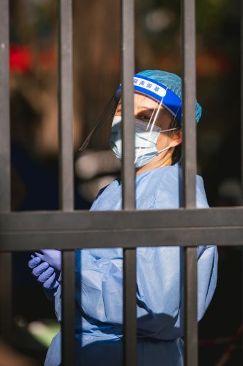 Covid health worker in full PPE gown mask gloves seen behind a gate or bars