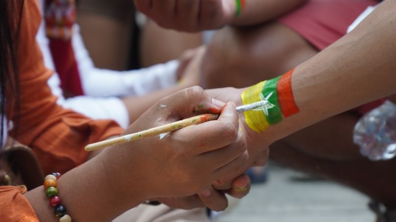 Hand painting the flag of Myanmar onto another person's wrist.(Unsplash)