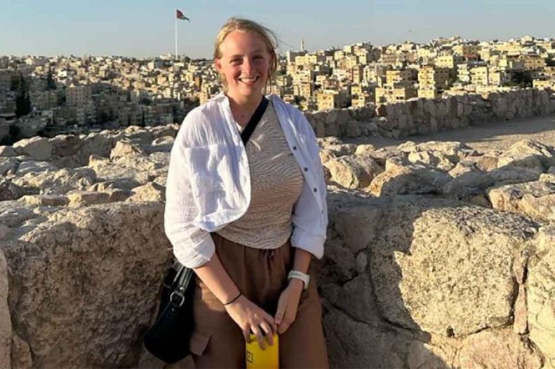 Margot Treadwell leans against a rock wall while smiling. 