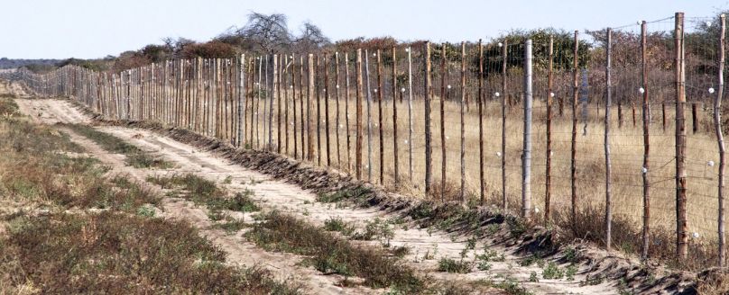 Wire and wood fence stretches across dry grasslands.