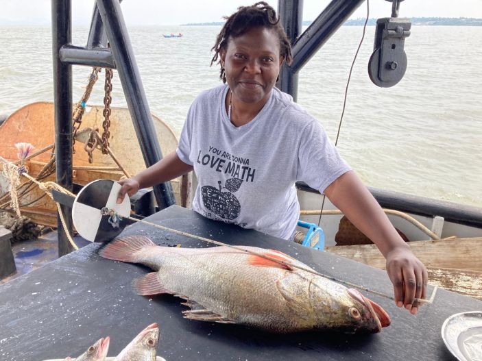 Angela Nankabirwa measures a large fish laying on a table.