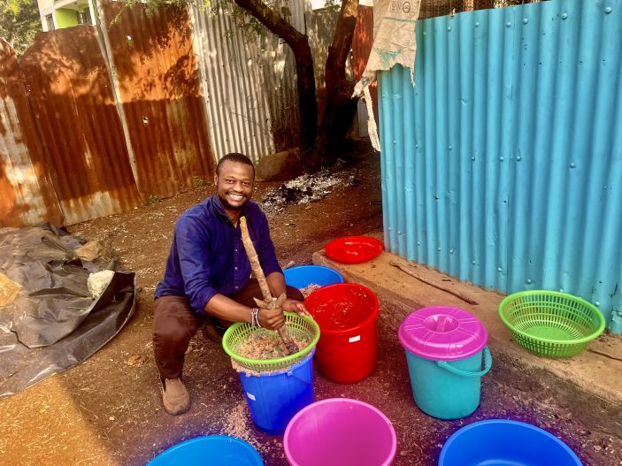 Jensen Njagi squats down next to colorful buckets. 