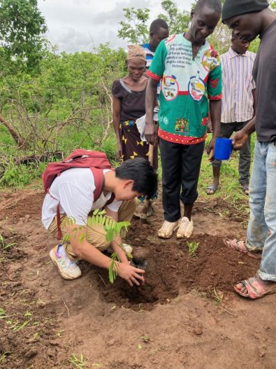 A Cornell student plants a tree next to collaborators standing nearby.