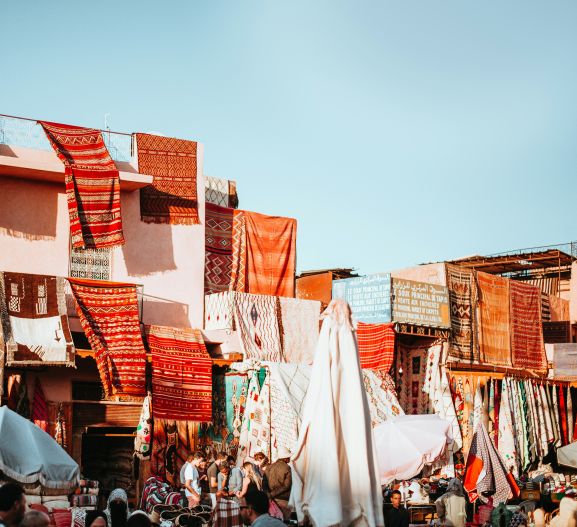 Bright orange and red rugs hang over buildings in Marrakesh.