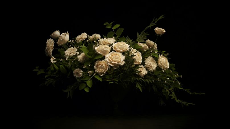 A photograph of a bouquet of white flowers against a dark background.