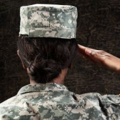 Woman soldier in military uniform stands at salute (seen from back of head)
