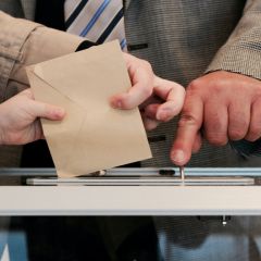 Hands holding placing a voting ballot into a receptacle.