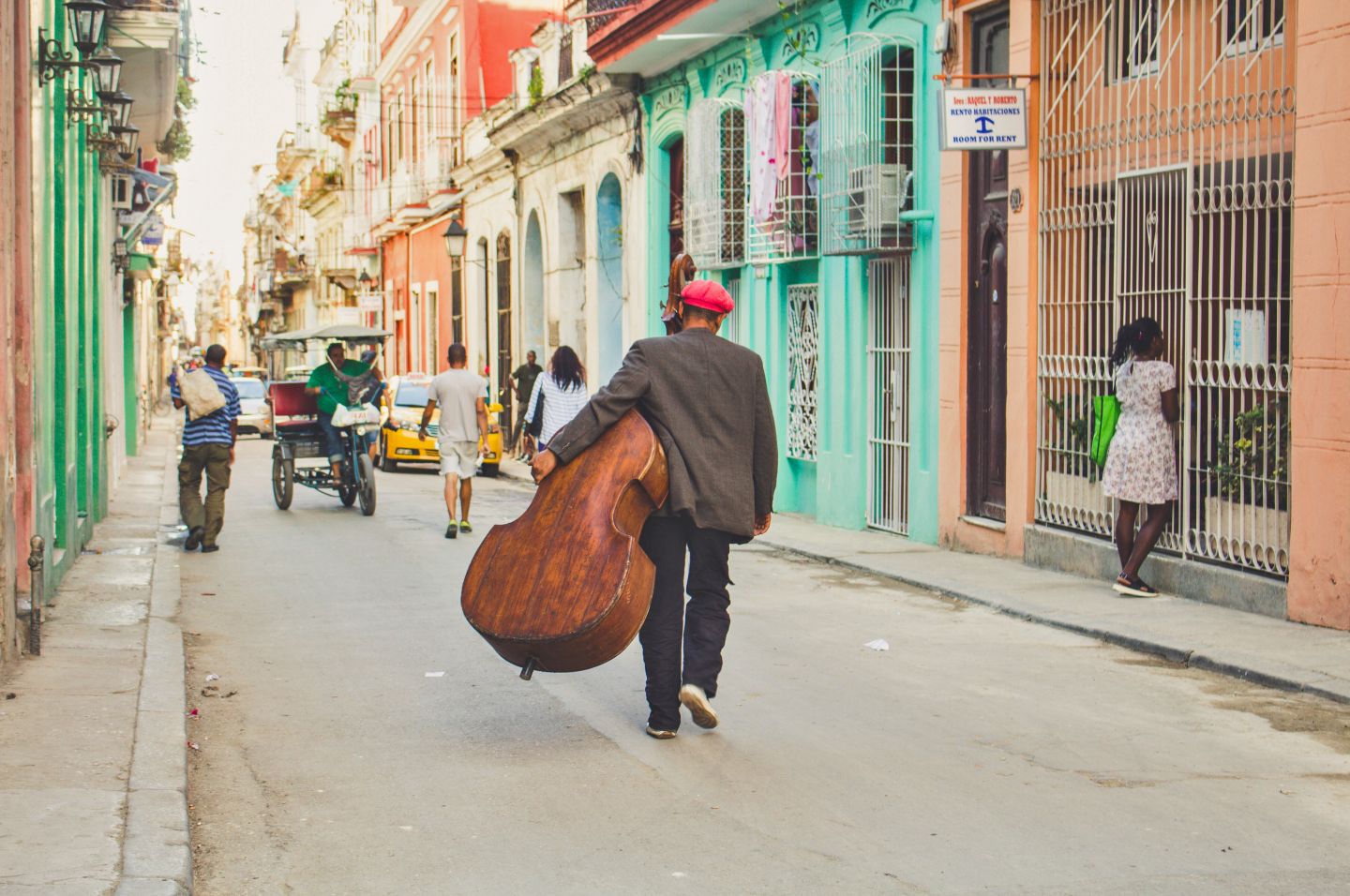 Man carrying cello down colorful streets of Havana, Cuba
