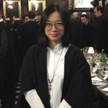 Xin Lei wears a black wrap white blouse glasses and has shoulder length hair