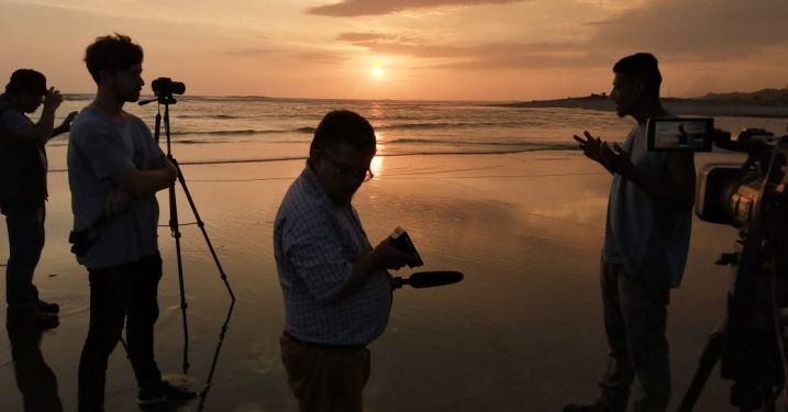 Man talking to people in front of sunset over water. John Kennedy at the estuarine border between Mexico and Guatemala filming an interview for his documentary Suchiate.