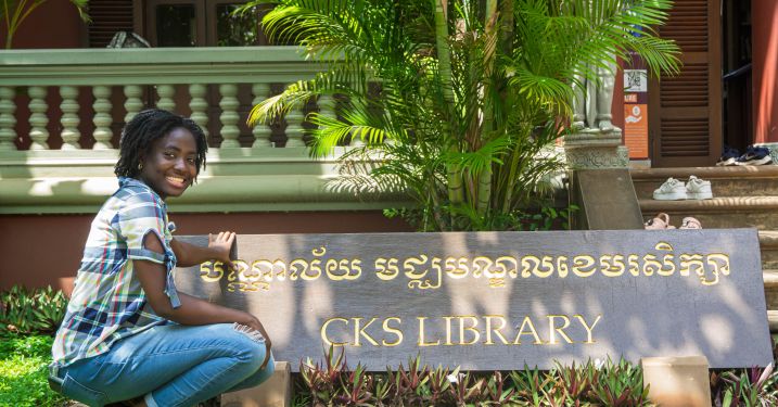 Global Intern Effi Acquaah poses for a photo next to a "CKS Library" sign in Cambodia.
