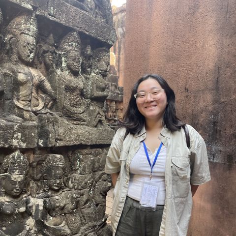 Emily Vo smiles and stands next to ancient carved architecture.