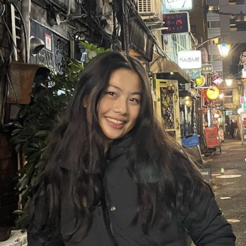 Chelsey Wang wearing a black jacket, smiling in front of a busy street.