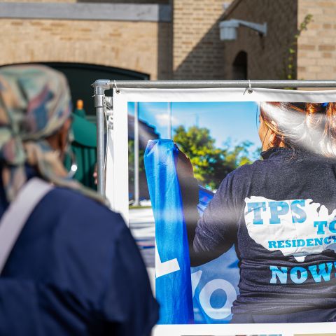 A person views a photo of a TPS worker wearing a "TPS to Residency Now" jacket.