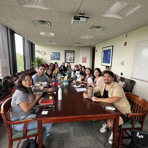 A group of students at Summer Pathways sit around a table, smiling and holding up migration books