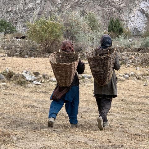 Two women walk along a dirt path carrying woven baskets