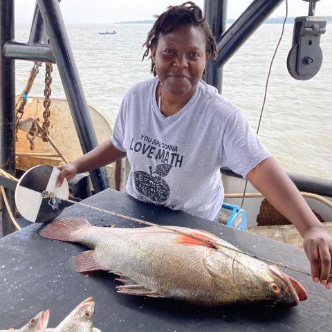 Angela Nankabirwa measures a large fish laying on a table.