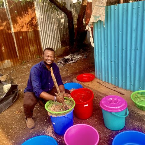 Jensen Njagi squats down next to colorful buckets. 