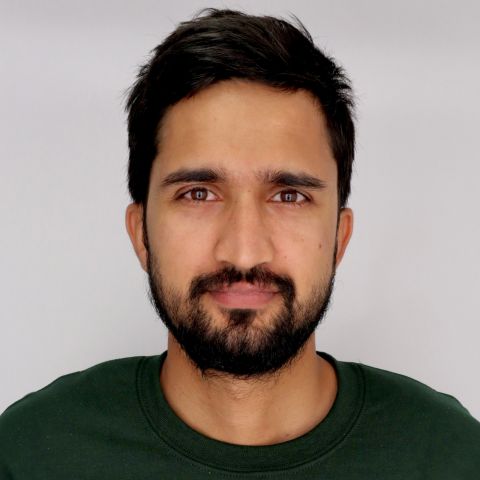 Man in green shirt standing in front of light gray background.