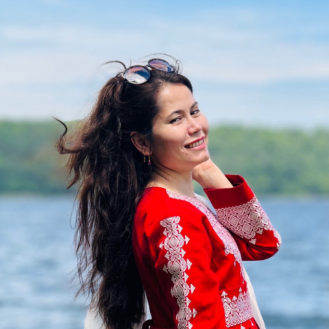 Woman in red shirt looks over shoulder at camera in front of waterfront.