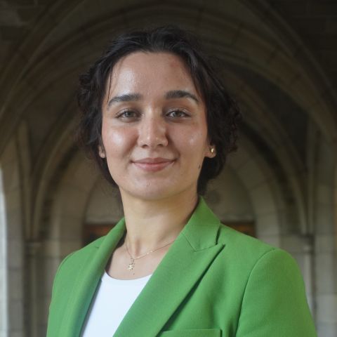 Woman in green blazer stands in stone hallway. 