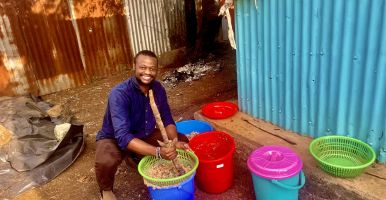 Jensen Njagi squats down next to colorful buckets. 