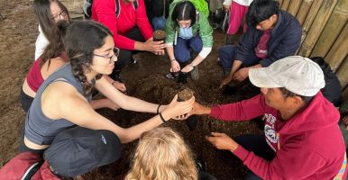 Laidlaw scholar hands a clump of a soil to an Ecuadorian man.